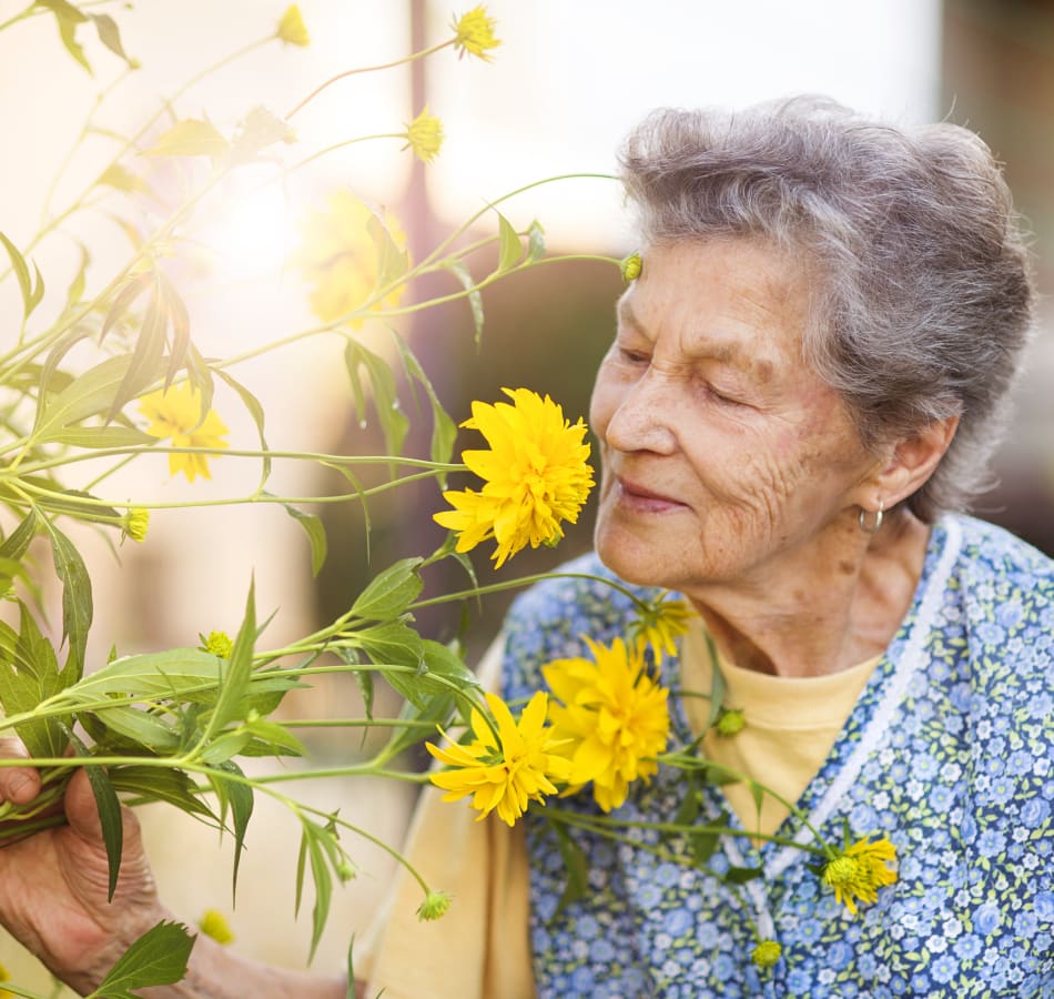 An elderly woman in a memory care program happily smells flowers.