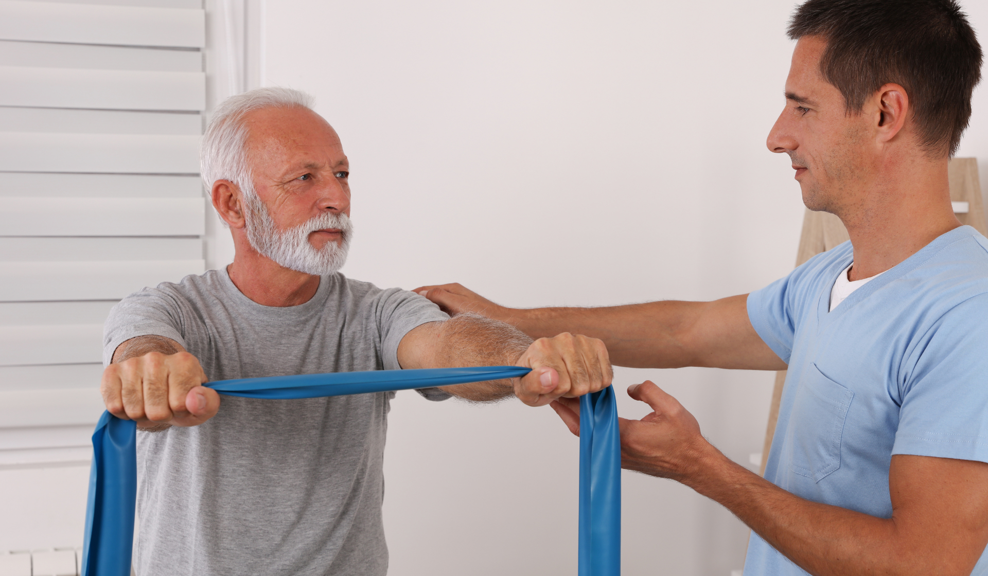 elderly man holding a rehabilitation stretching band with a nurse aid beside him